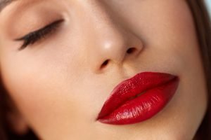 Beauty Woman Face With Professional Makeup And Sexy Red Lips. Closeup Of Beautiful Model Girl With Smooth Soft Facial Skin And Cosmetic Lipstick On Plump Full Lips. Cosmetics Concept. High Resolution